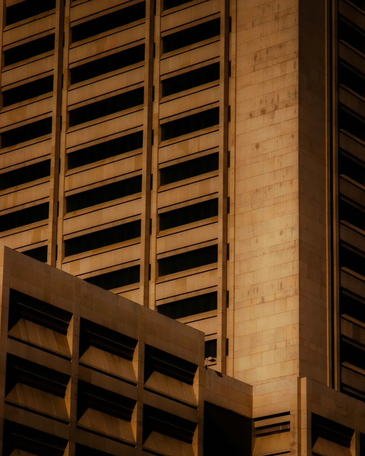 The facade of a tall modernist building in warm golden light, rows of dark horizontal windows receding across its concrete face.