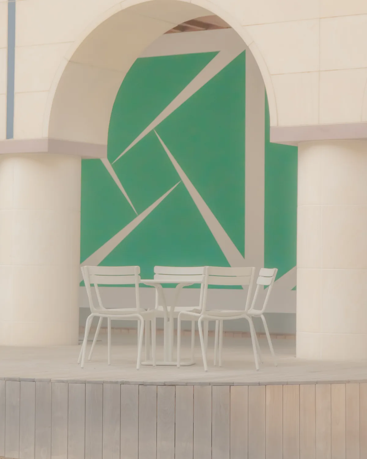 White chairs and a round table set beneath a stone archway, backed by a bold green geometric mural between two columns.
