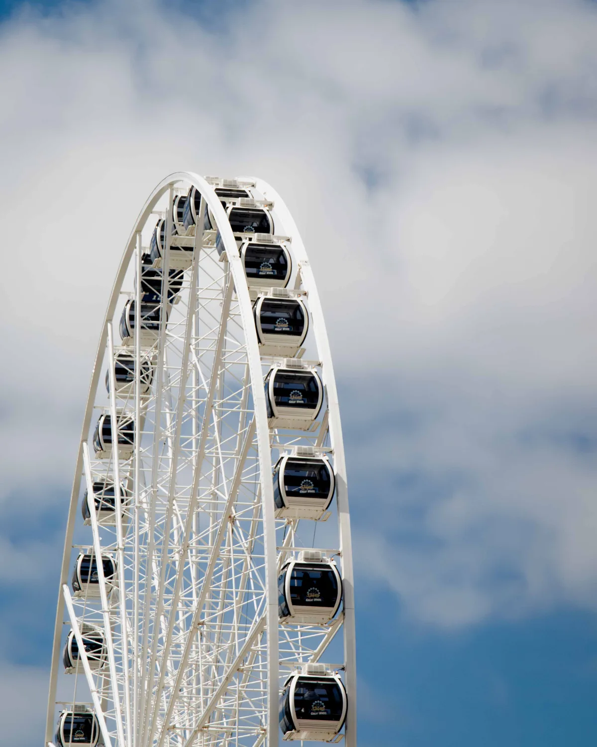 A white Ferris wheel rising into a blue sky scattered with soft clouds, its enclosed gondolas curving out of frame.