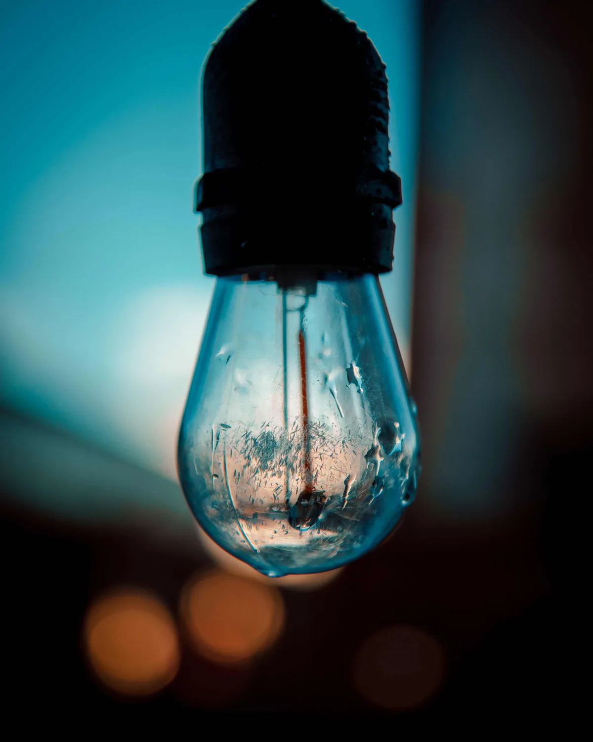 A hanging Edison-style bulb with an unlit filament and condensation clouding the glass, warm blurred lights behind it.